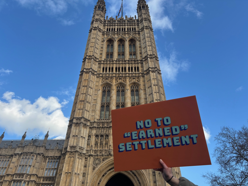 Someone holding a sign that says 'No to earned settlement' outside of Parliament